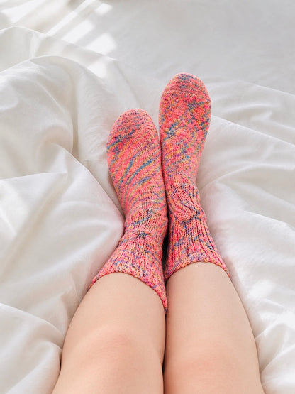 Person wearing pink and gray patterned socks on a white bed.