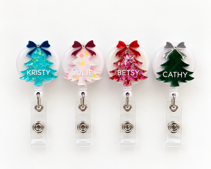 Four personalised Christmas tree badge reels in teal glitter, pastel polka dot, pink and red glitter and green marble, each with a bow and a name