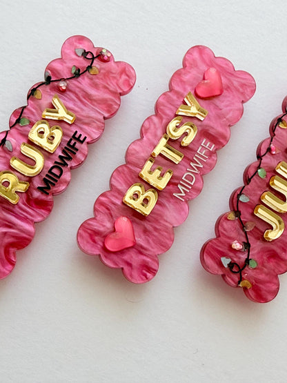 Close-up of pink glitter Christmas lights midwife name badges with raised gold names
